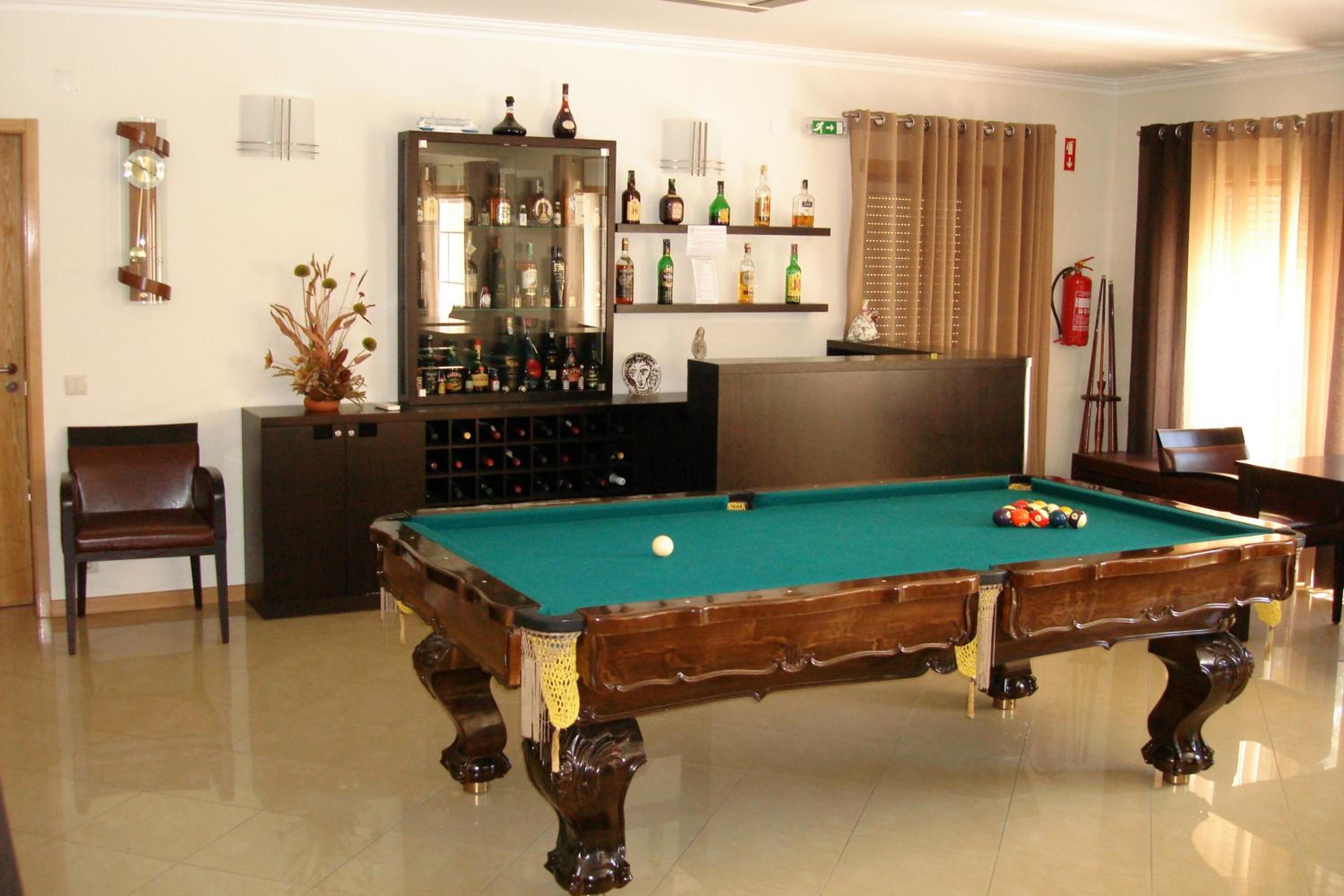 A billiards room with a pool table, chairs, a cabinet with bottles, a mirror, and a fire extinguisher.