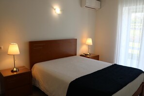 A hotel room with a single bed, two bedside tables with lamps, a wooden headboard, an air conditioning unit, and a window with sheer curtains. - Hotel Solar Das Laranjeiras (Vale de Cambra)