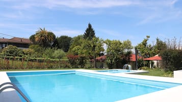 A clear blue swimming pool with a white deck, surrounded by lush greenery and trees.