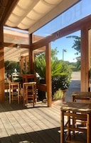 Una terraza de madera al aire libre con una zona de estar cubierta, un letrero con la palabra 'HOH', y vistas a un estacionamiento y áreas verdes.
