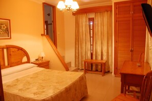 Quarto de hotel com cama, escrivaninha, cadeira, mesa de cabeceira e espelho.