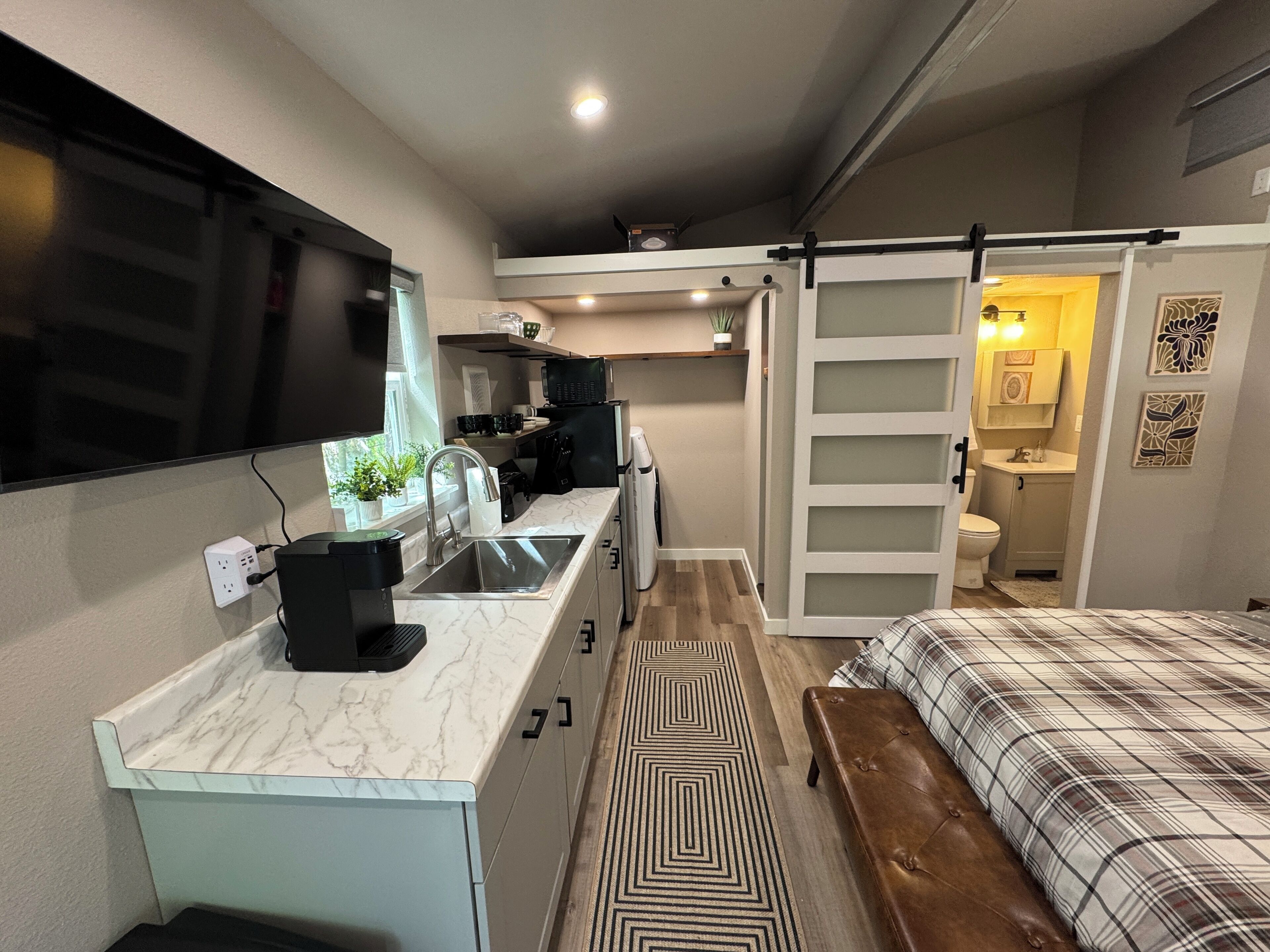 Een compact studio-appartement met kitchenette, een bed, een badkamer en een schuifdeur naar een klein balkon.