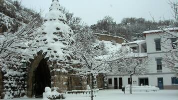 A snow-covered courtyard with a stone archway, a snow-covered tree, and a building with multiple windows.