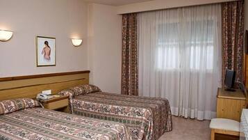 A hotel room with two beds, a desk, a chair, a television, and a window with curtains.
