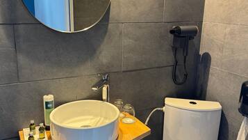 Ein modernes Badezimmer mit einem runden Spiegel, einem weißen Waschbecken, einer Toilette und einem Föhn an der Wand.