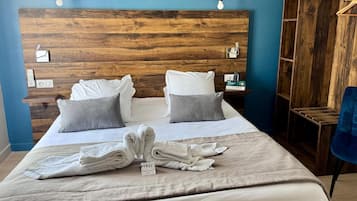 A hotel room with a wooden headboard, two bedside tables with lamps, a bed with white bedding and gray pillows, and a blue chair.