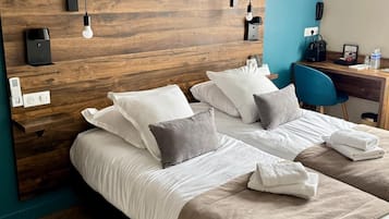 A hotel room with a wooden headboard, two beds, a desk with a chair, and a blue accent wall.