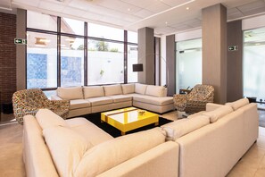 Eine moderne Lobby mit einem Ecksofa, gemusterten Sesseln, einem zentralen Couchtisch und großen Fenstern.