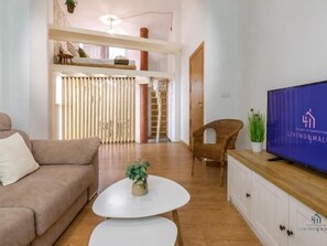 Uma sala de estar moderna com um sofá, uma mesa de centro e uma televisão. Há uma escada que leva a um andar superior.