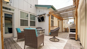 Un espace patio aménagé avec des meubles en osier, un barbecue et un téléviseur fixé au mur.