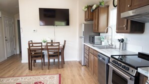 A modern kitchen with wooden cabinets, a built-in microwave, a stainless steel refrigerator, and a flat-screen TV mounted on the wall.