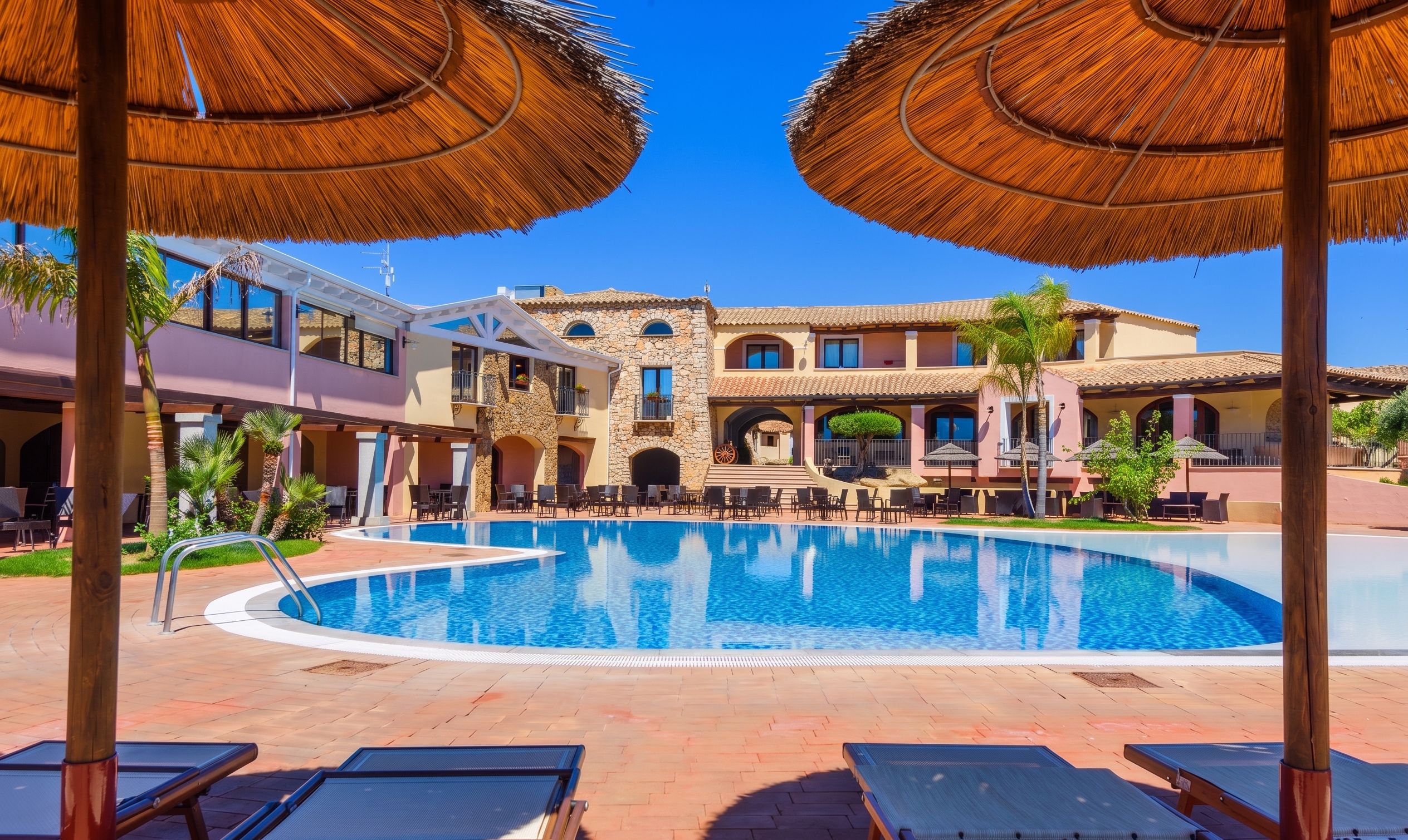 A pool area with lounge chairs, a swimming pool, and a building with a stone facade and multiple balconies.