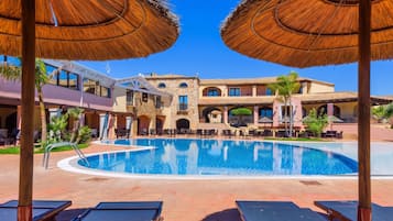 A pool area with lounge chairs, a swimming pool, and a building with a stone facade and multiple balconies.