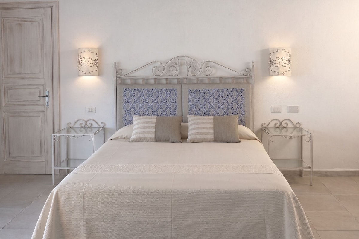 Une chambre à coucher avec un lit, deux tables de chevet, une porte et un papier peint à motifs.
