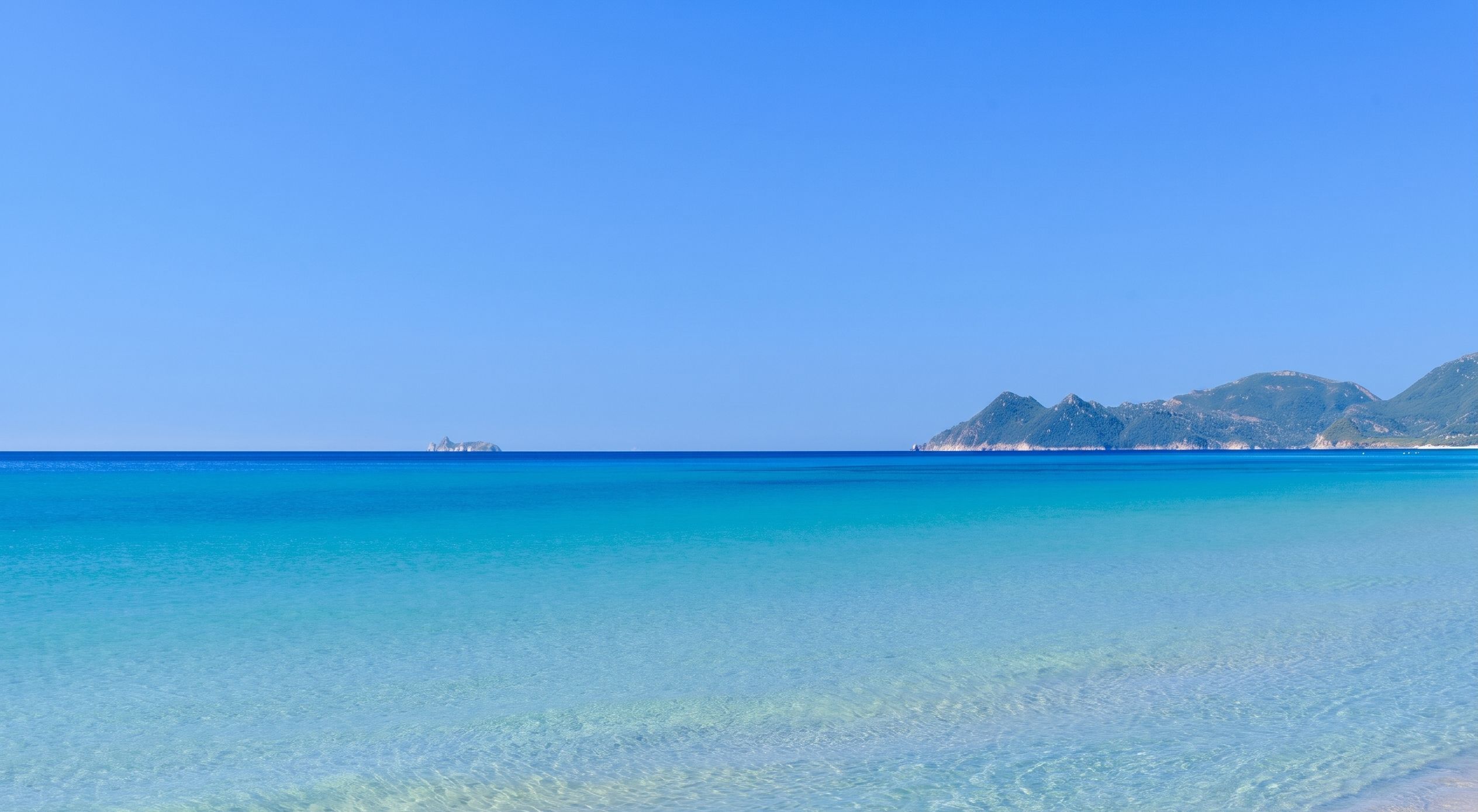 A clear blue sea with a distant island and mountains.
