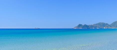 A clear blue sea with a distant island and mountains.