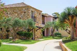 A stone building with a tiled roof, a paved pathway, and surrounding greenery. - Valtur Sardegna Eos Costa Rei (Muravera)