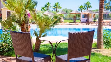 A poolside area with wicker chairs, a small round table, and palm trees.