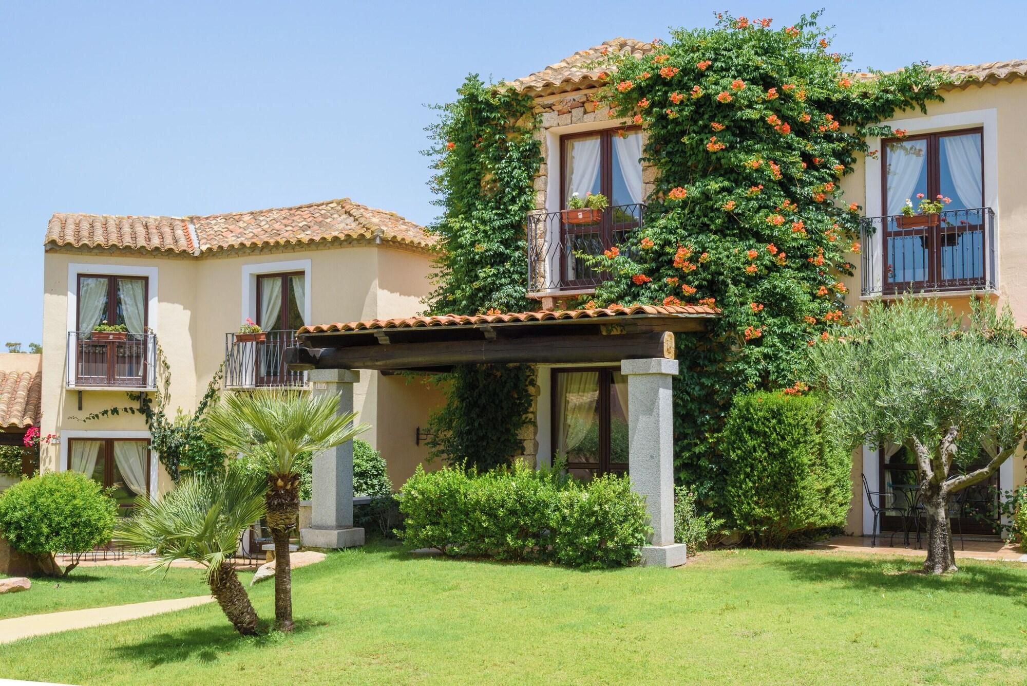 Un edificio con tetto in tegole, un portico coperto e un giardino con palme e arbusti.