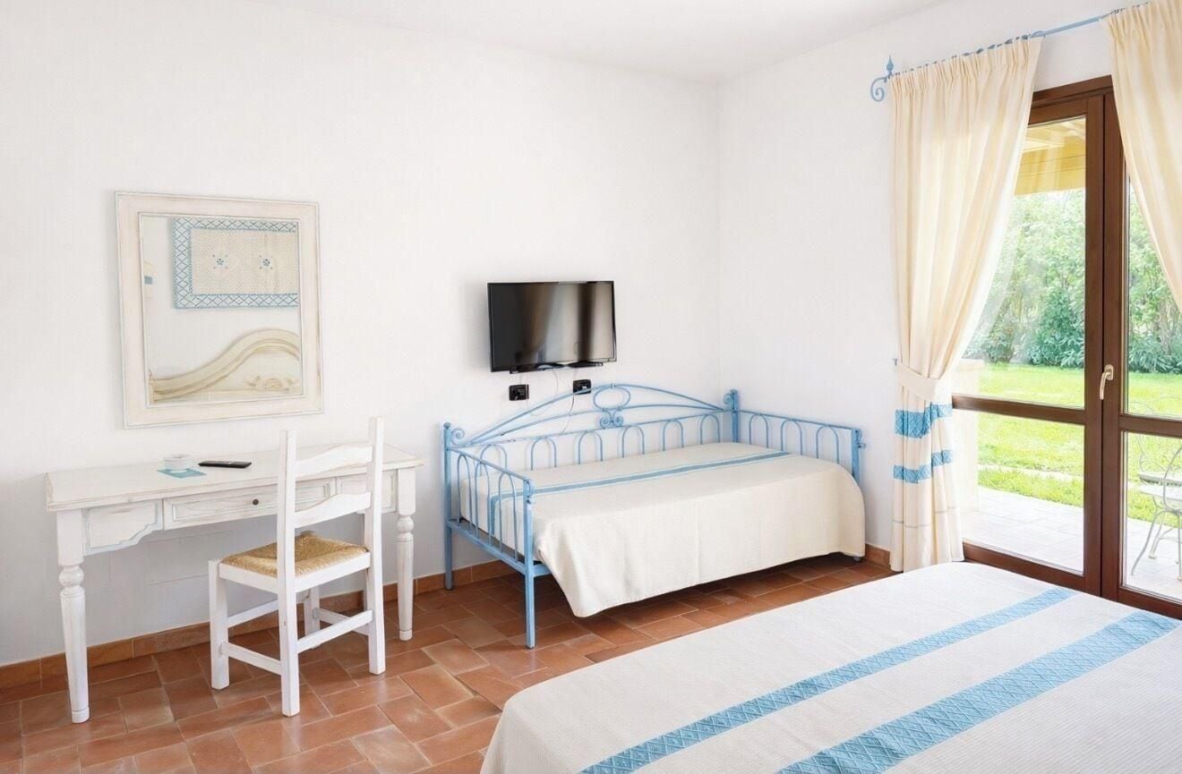 A bedroom with a bed, a desk, a chair, a television, and a window with curtains.
