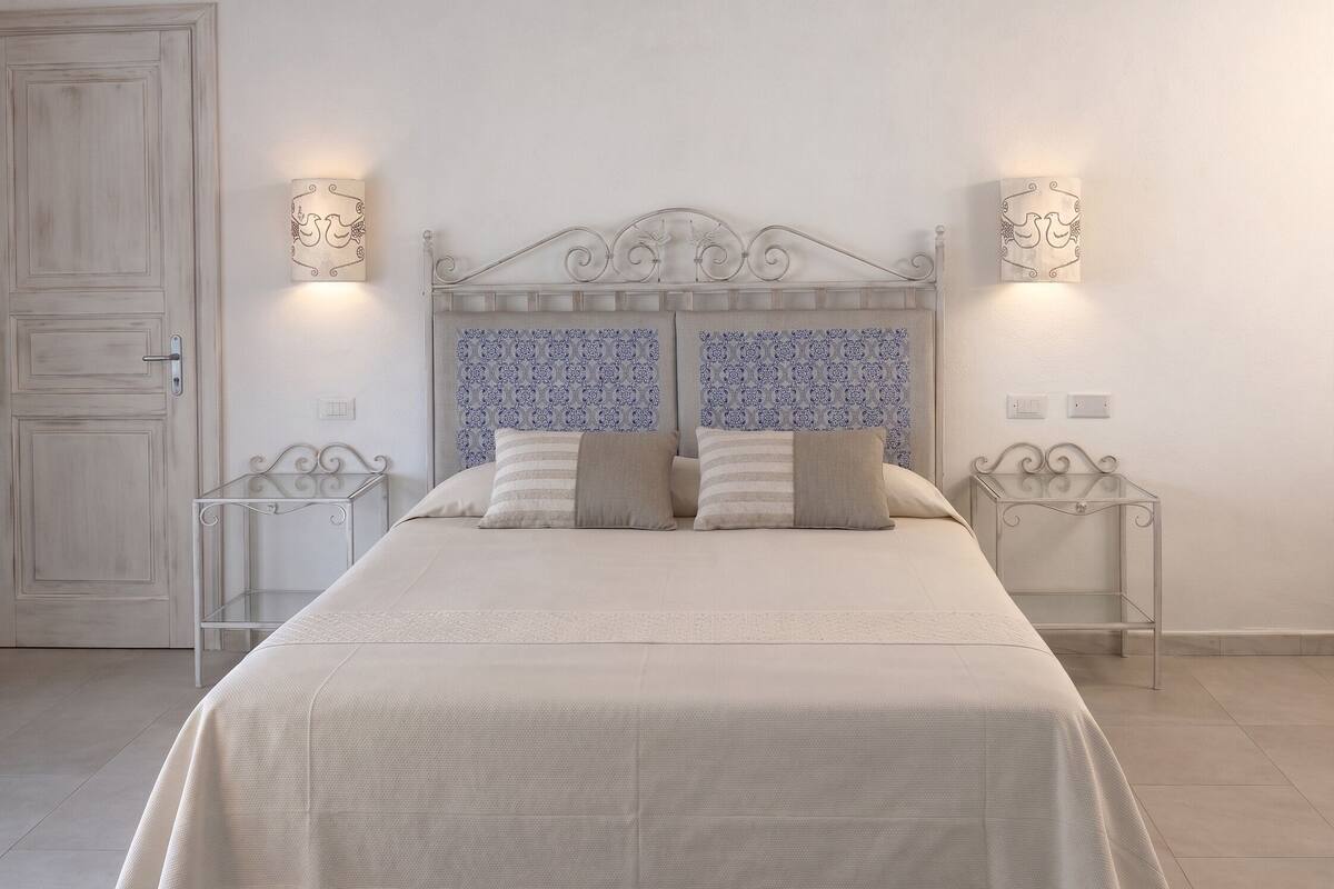 Un dormitorio con cama, dos mesitas de noche, una puerta y papel tapiz estampado.