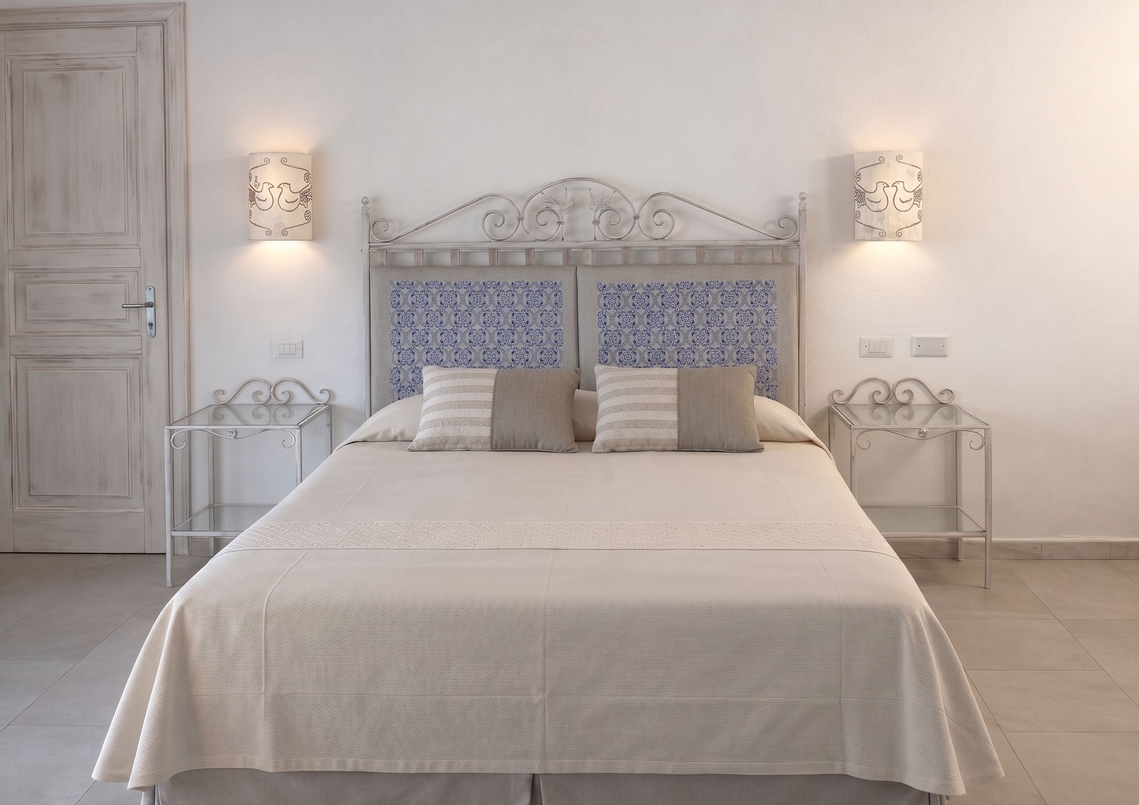 Une chambre à coucher avec un lit, deux tables de chevet, une porte et un papier peint à motifs.