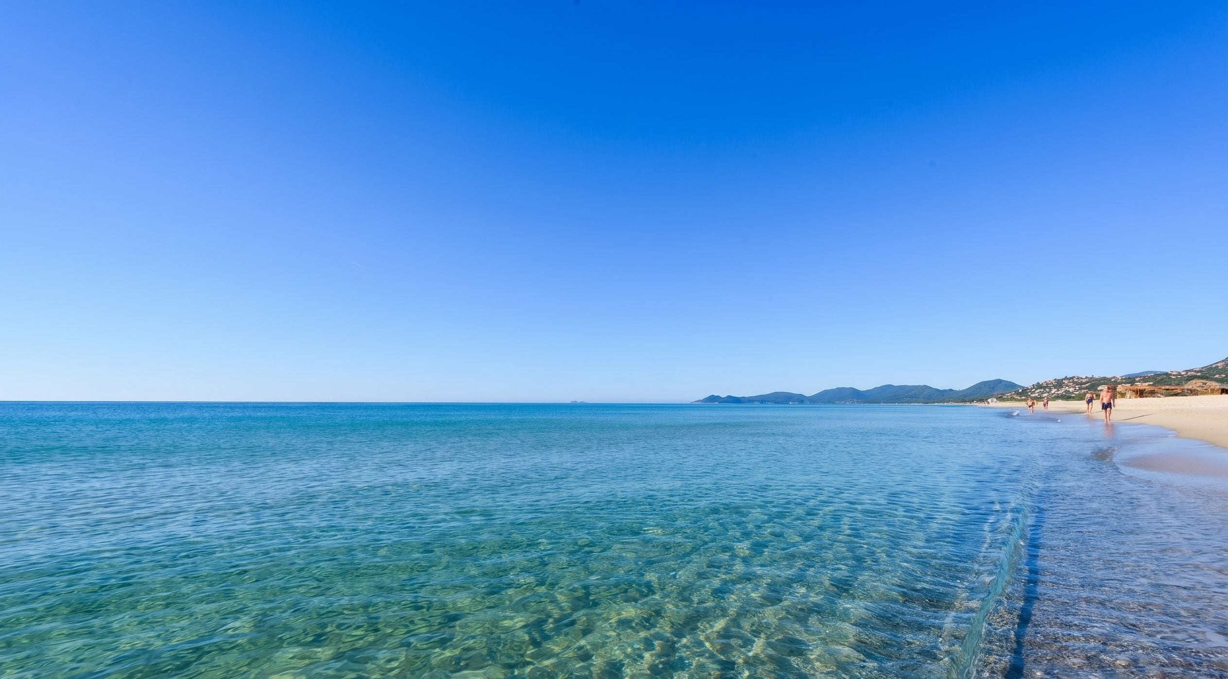 A beach with clear water, sandy shore, and distant mountains.