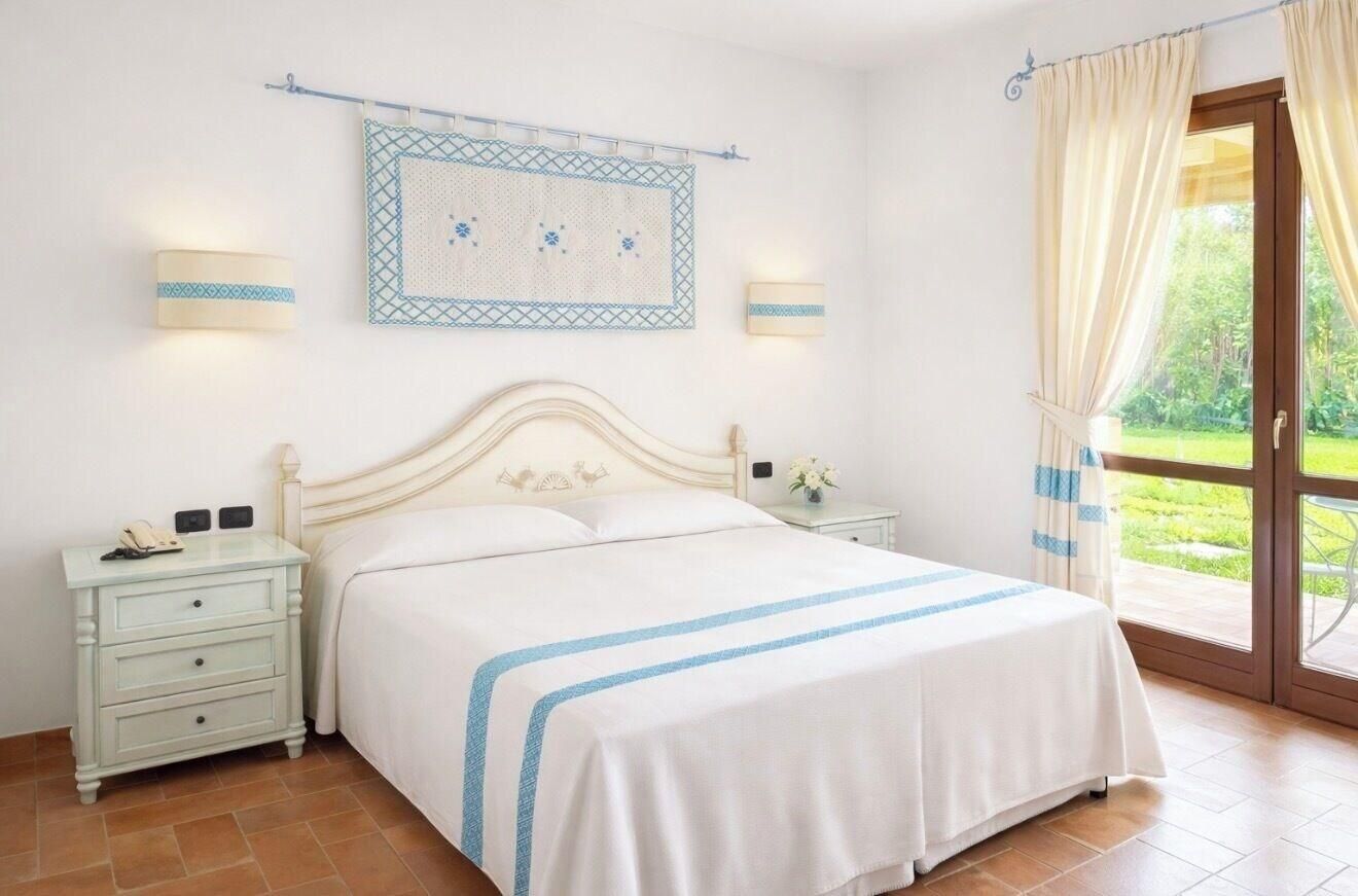 A bedroom with a bed, nightstands, a wall-mounted light, and a window with curtains.