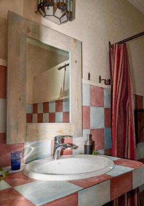 A bathroom with a large mirror, a round sink, a shower curtain, and a tiled wall with a checkered pattern. - Atlas Aura (Marrakech)