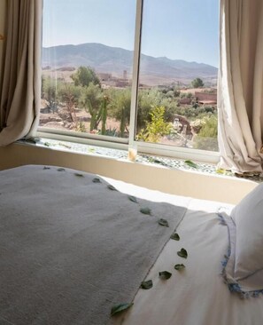 A bedroom with a large window, a bed with a white sheet, and a view of a desert landscape. - Atlas Aura (Marrakech)