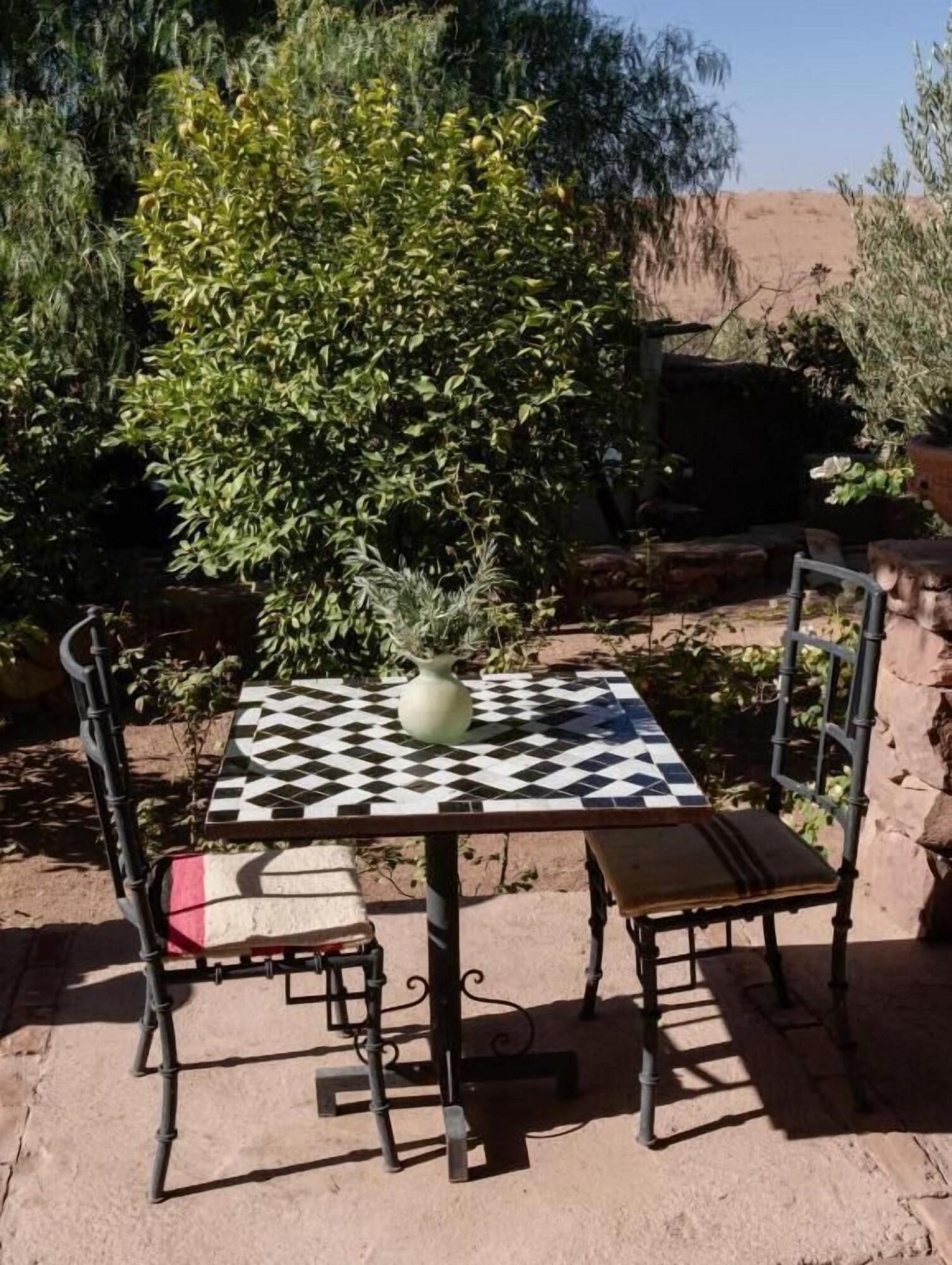A square table with a checkered tablecloth, a vase, and two chairs with cushions.