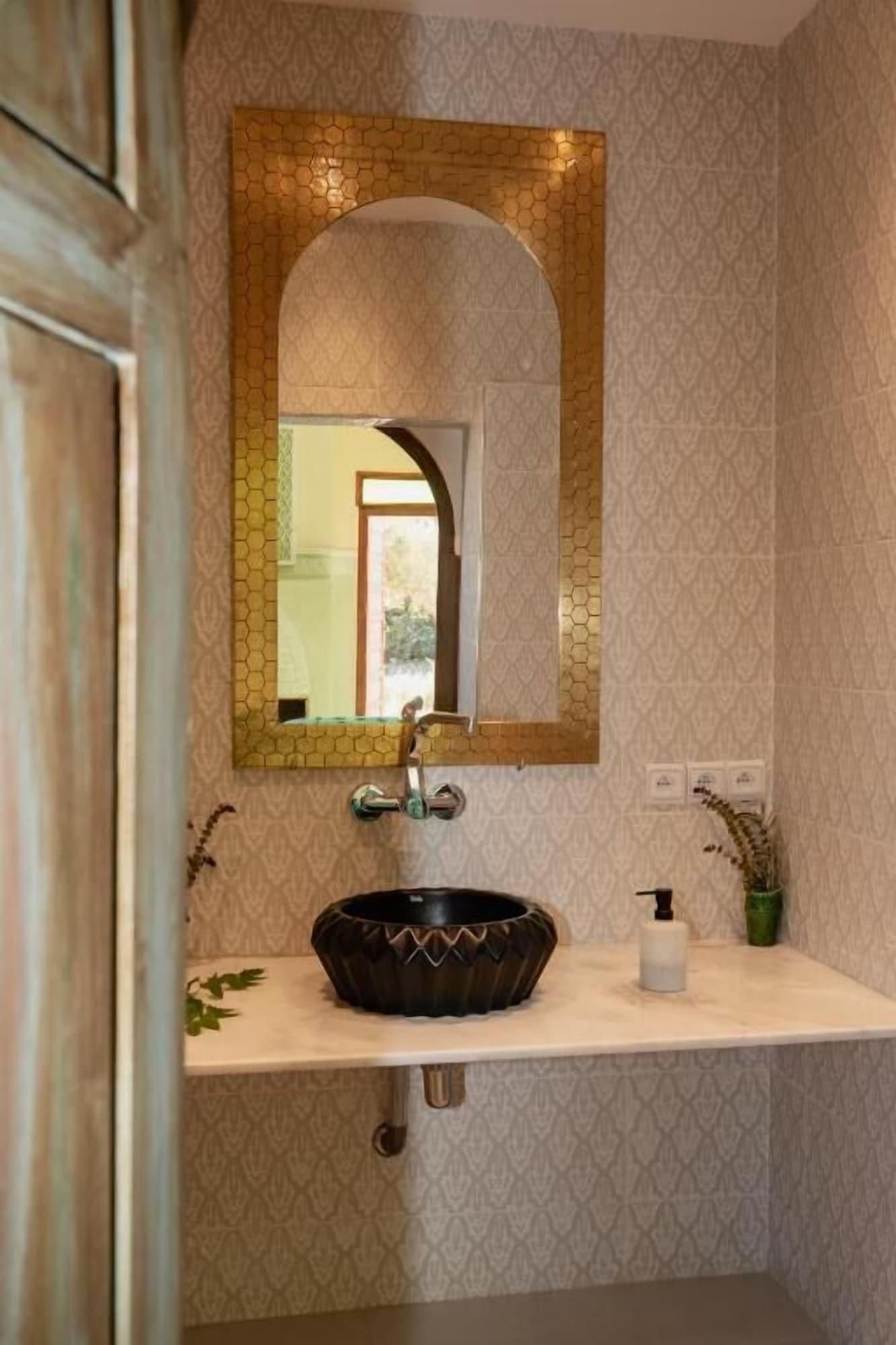 A bathroom with a round vessel sink, a mirror with a hexagonal frame, and patterned wallpaper.