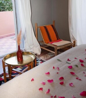 A bedroom with a bed, a chair, a small table with a bottle, and a view of the outside. - Atlas Aura (Marrakech)