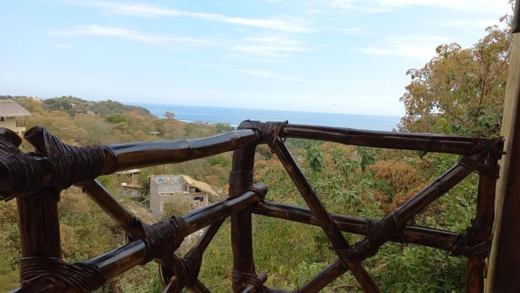 A bamboo fence overlooking a coastal landscape with vegetation and a distant view of the sea.
