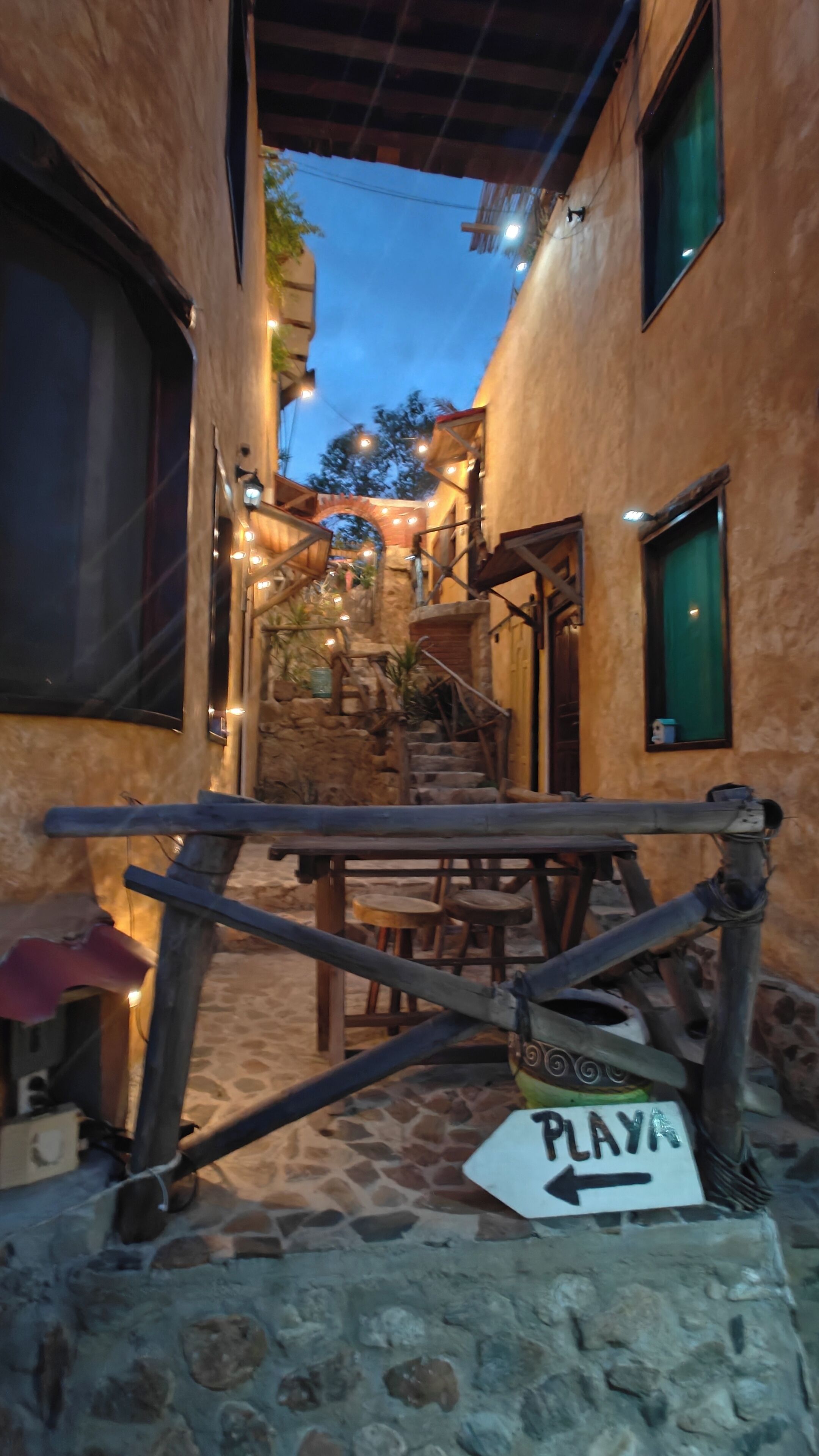A narrow alleyway with stone walls, a wooden gate, and a sign that reads 'PLAY'.