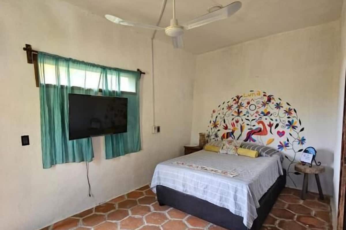 Une chambre à coucher avec un lit, un ventilateur de plafond, une télévision et une tête de lit à motifs.