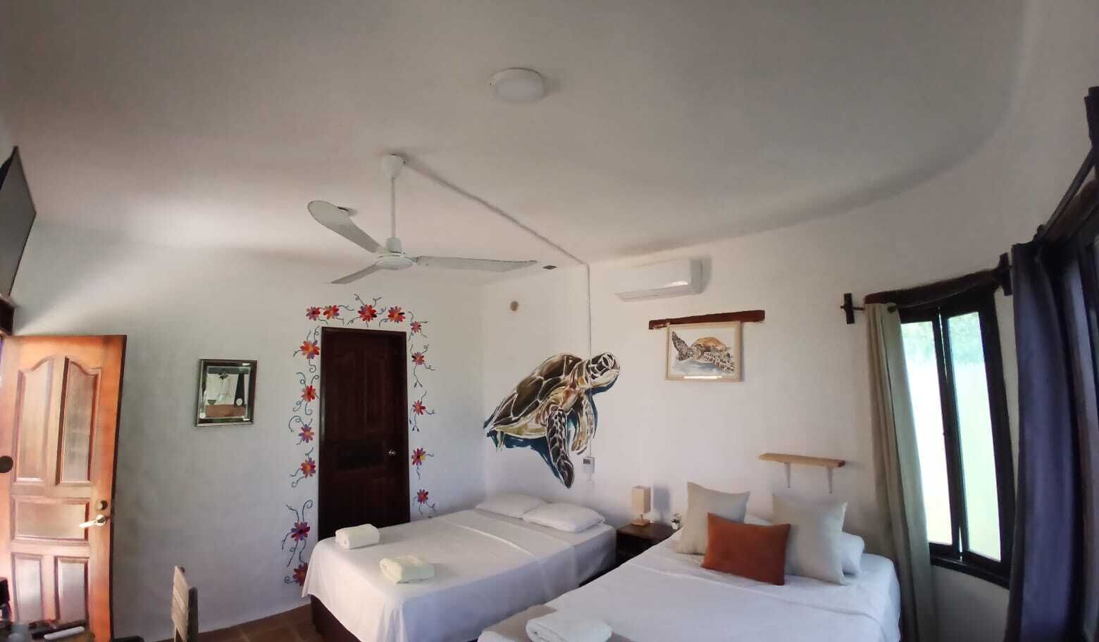 Quarto com duas camas, um ventilador de teto, uma porta e um mural na parede.