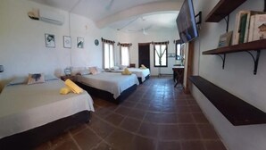 Habitación de hotel con tres camas, un televisor, una estantería con libros y suelo de baldosas.