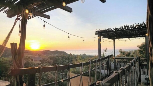 Una pérgola de madera con luces colgantes, con vista a un paisaje pintoresco y una vista del atardecer.