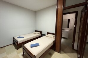 Una stanza con due letti singoli, una porta in legno e un tavolino.
