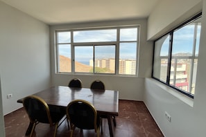 A dining area with a table and chairs, large windows with a view of buildings and hills.