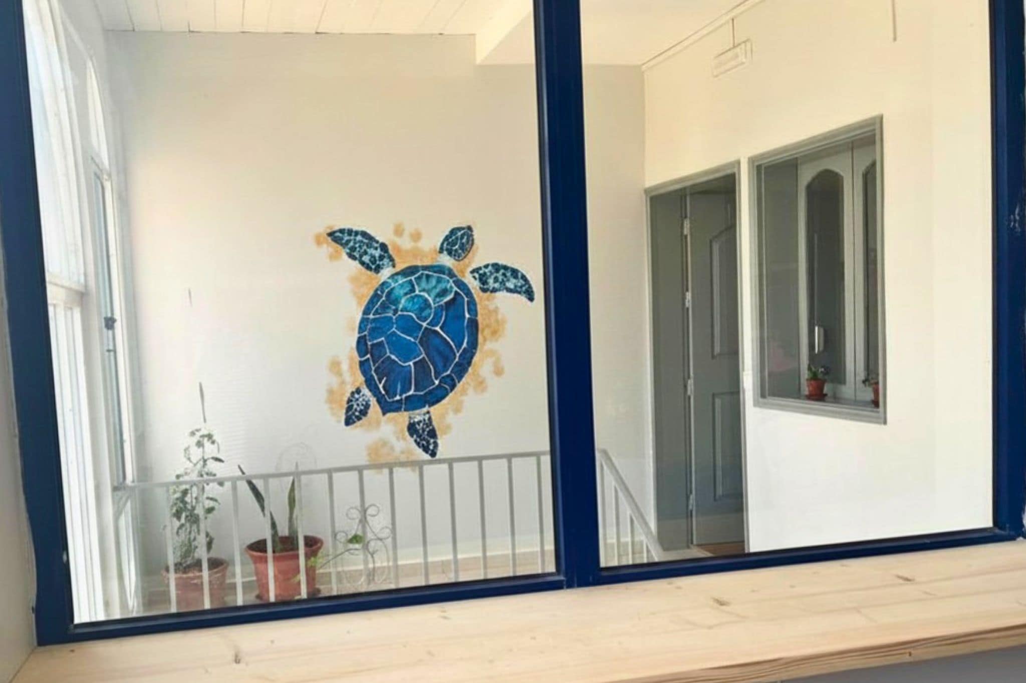 Une pièce dotée d’une grande fenêtre, d’une porte et d’un mur orné d’une fresque représentant une tortue de mer.