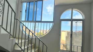 A staircase with a metal railing leading to a balcony with large windows offering a view of buildings and a crane.