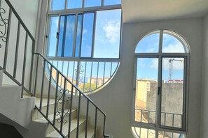 A staircase with a metal railing leading to a balcony with large windows offering a view of buildings and a crane. - Residencial Alto Do Fortim (São Vicente)