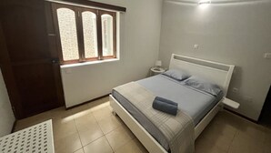 Une chambre à coucher avec un lit, une table de chevet, une lampe et une fenêtre avec des rideaux.