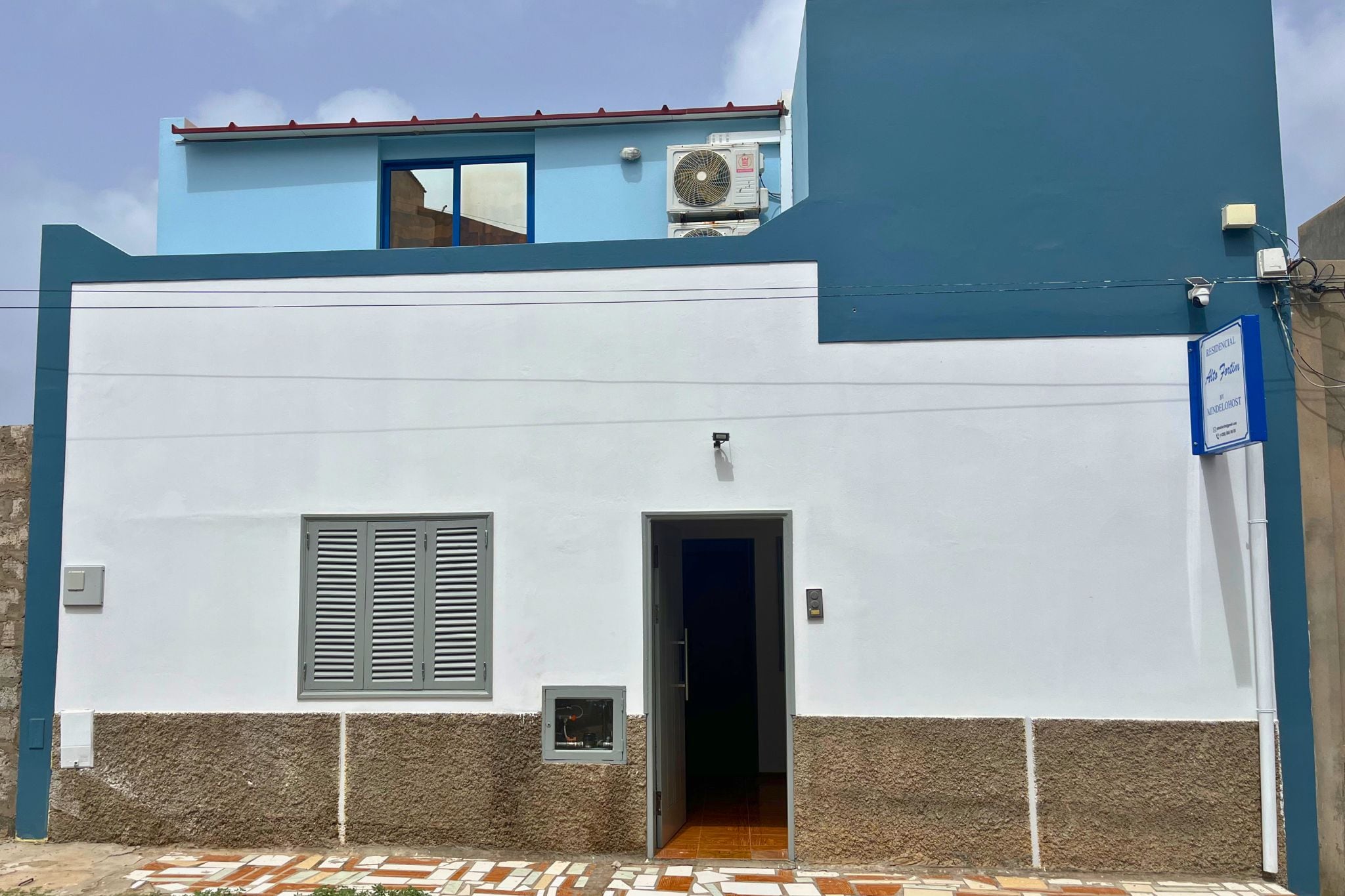 Un edificio residencial con fachada blanca, una sola puerta y una ventana pequeña con persianas.
