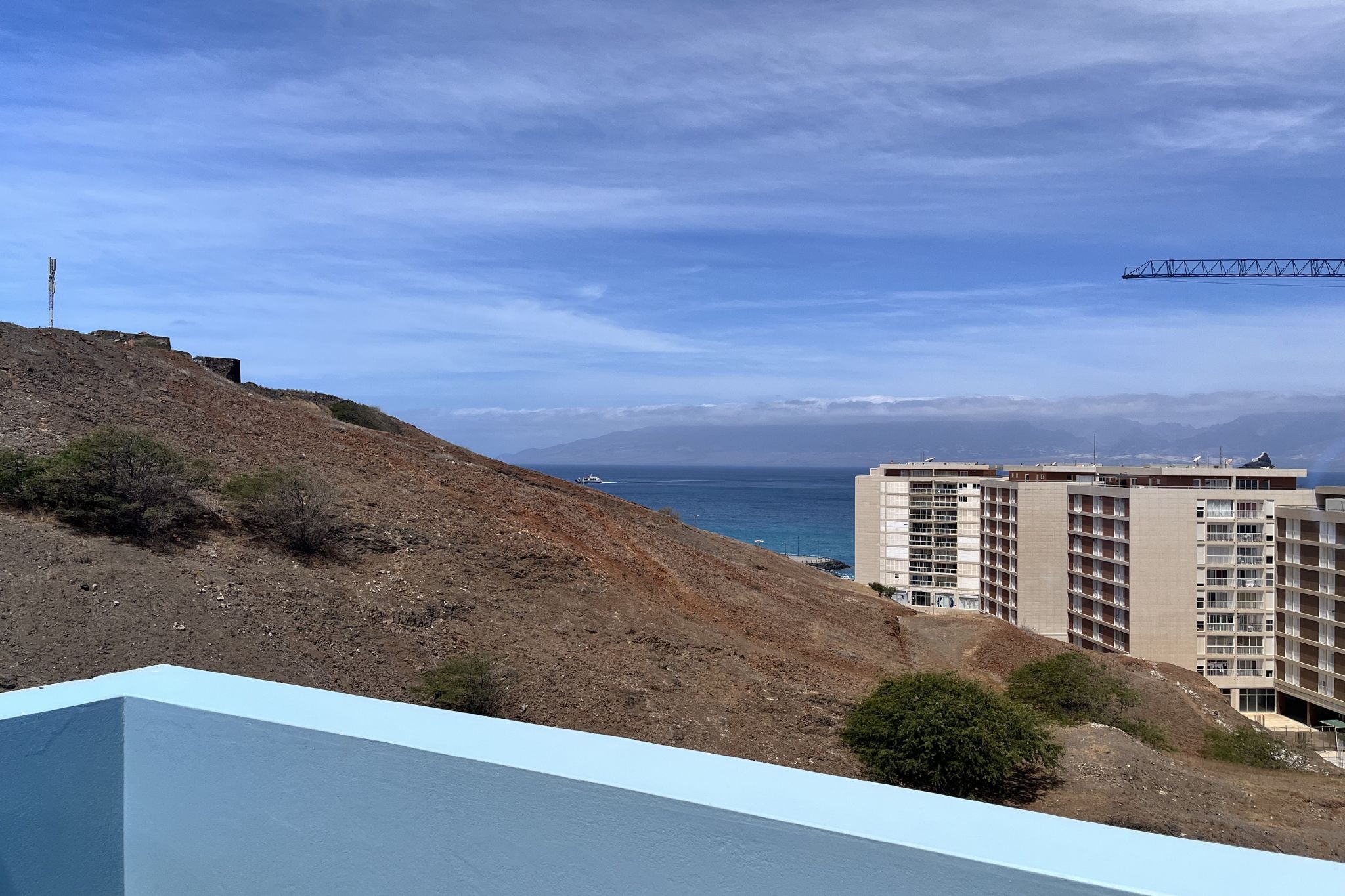 A coastal view with a building, a hill, and a clear sky.