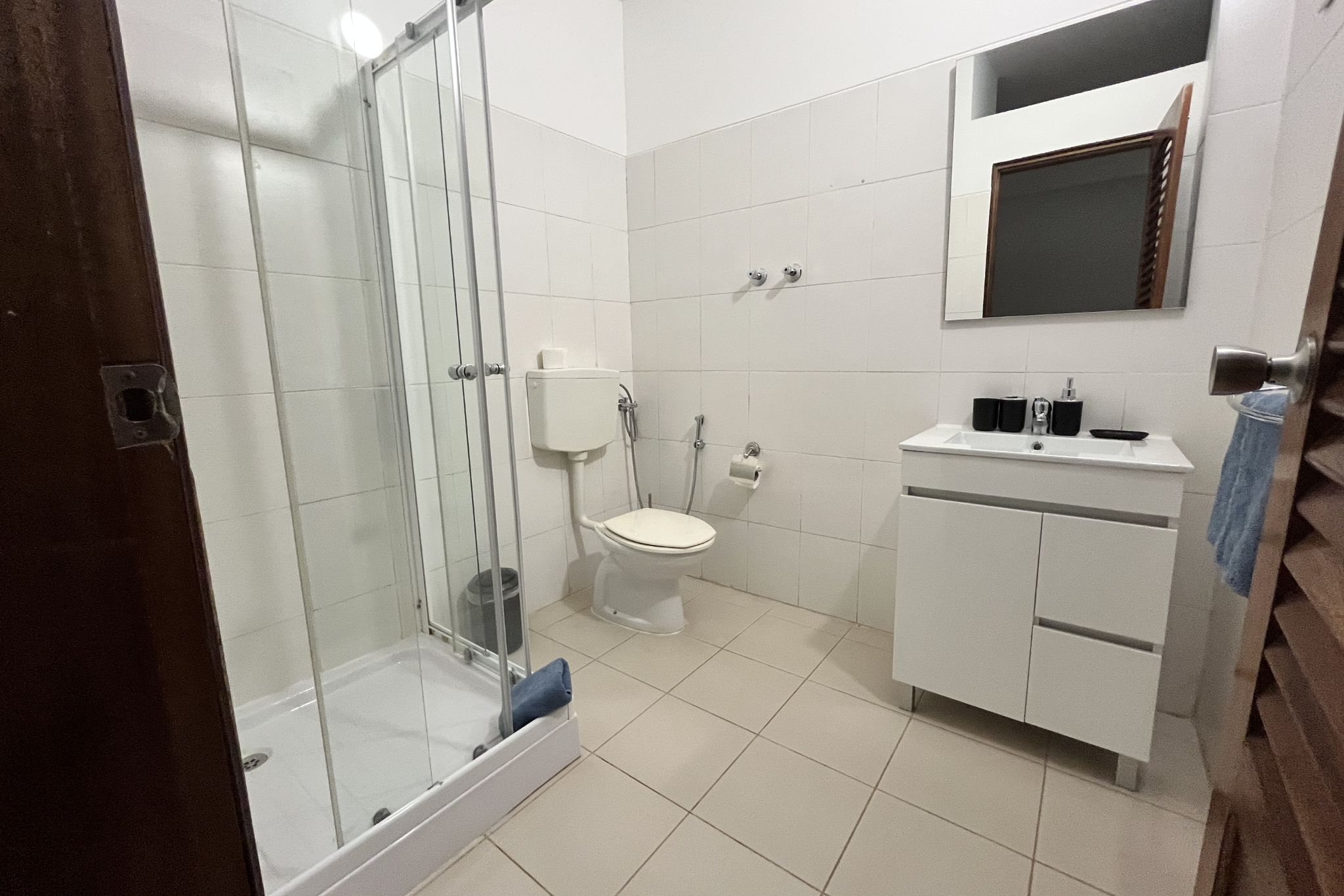 Un baño con ducha de vidrio, inodoro y lavamanos con espejo.