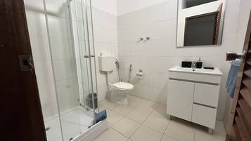 Un baño con ducha de vidrio, inodoro y lavamanos con espejo.