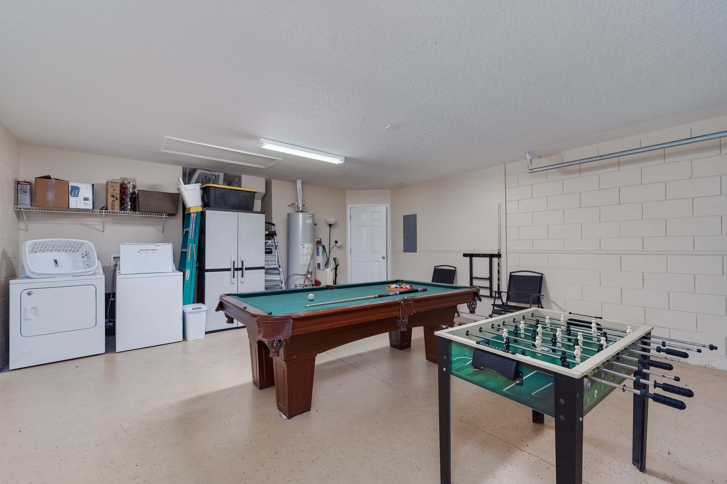 A recreational room with a pool table, foosball table, and a refrigerator.